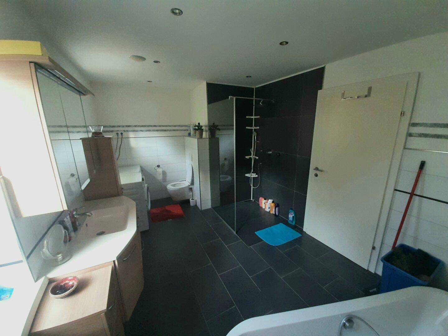 Modernes Badezimmer mit dunklen Fliesen, begehbarer Dusche und Badewanne.