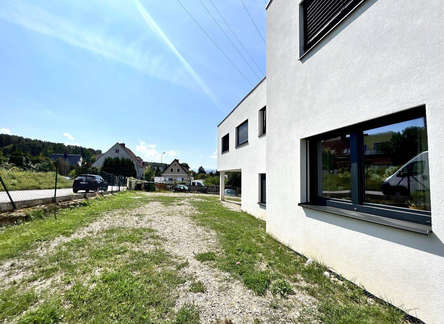Seitenansicht eines modernen Neubaus mit weißer Fassade und dunklen Fensterläden.