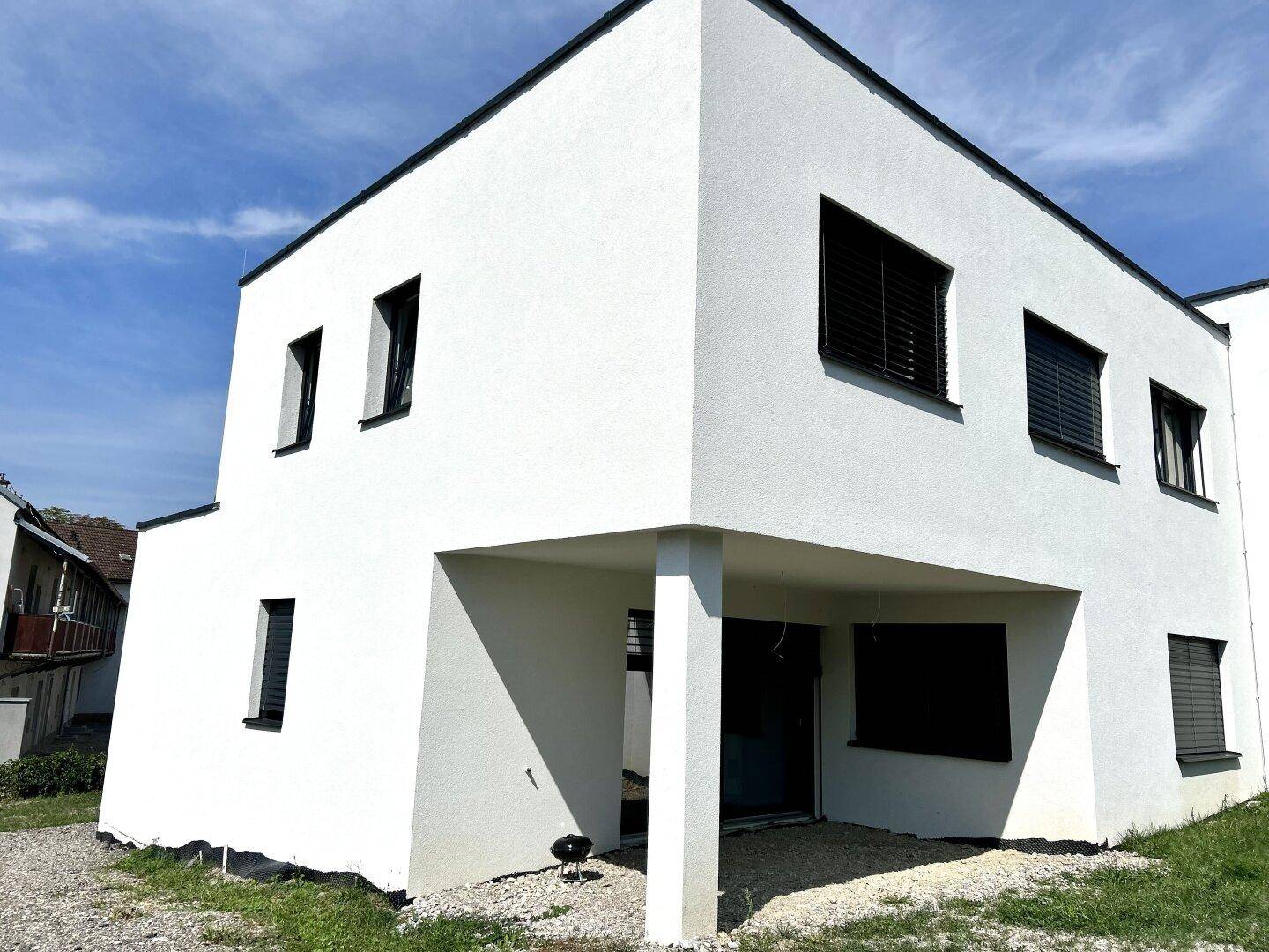 Moderner Neubau mit weißer Fassade, Flachdach und überdachtem Eingangsbereich.