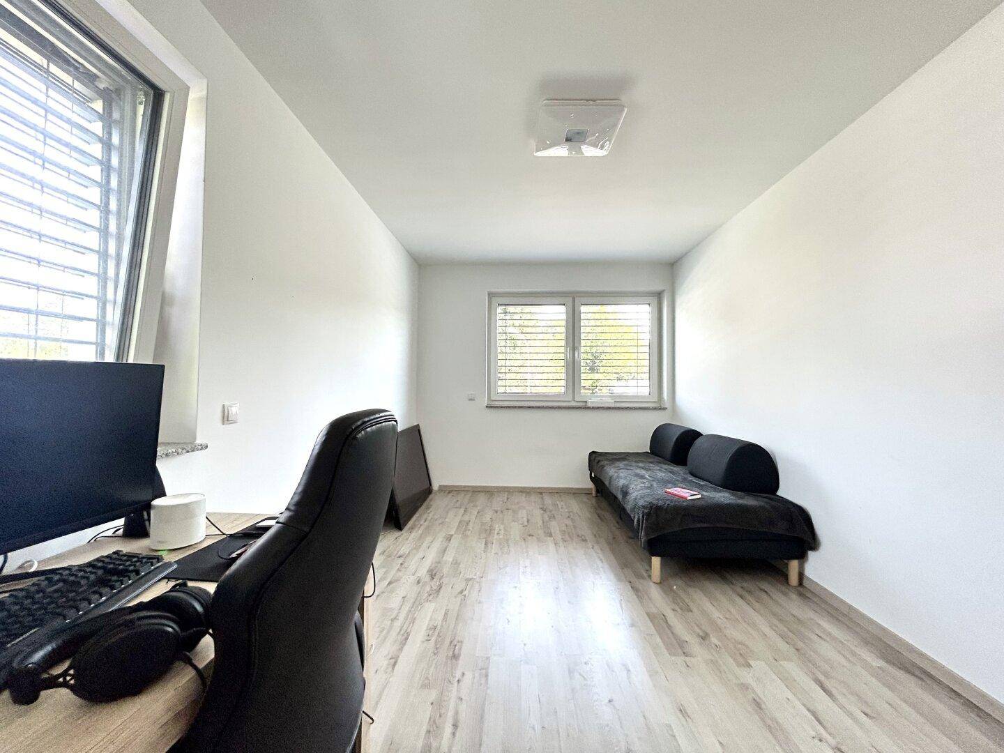 Helles Arbeitszimmer mit Laminatboden, großem Fenster und einem Schreibtischbereich.