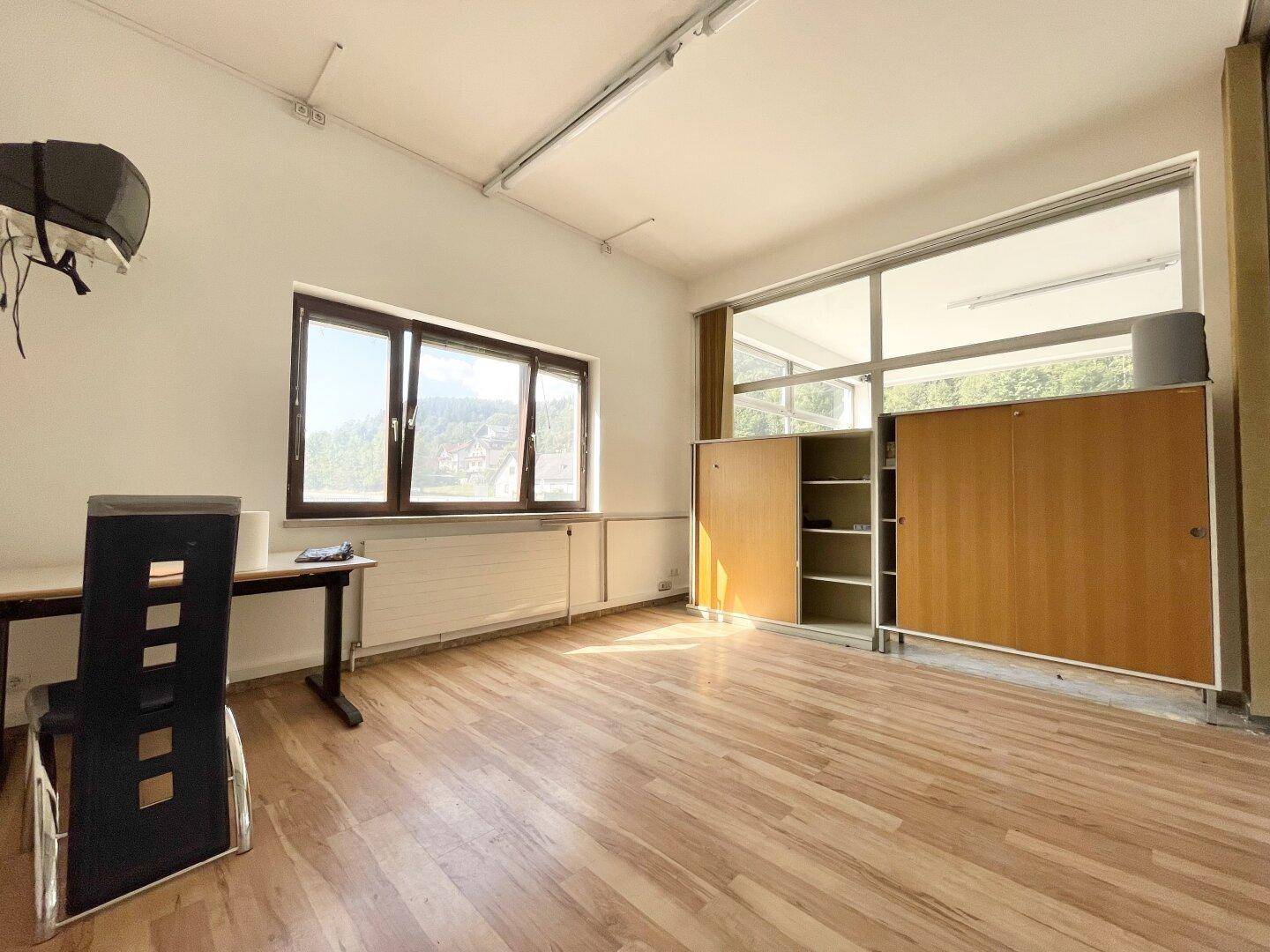 Helles Büro mit Laminatboden, großem Fenster und einfacher Möblierung, bietet viel Tageslicht.