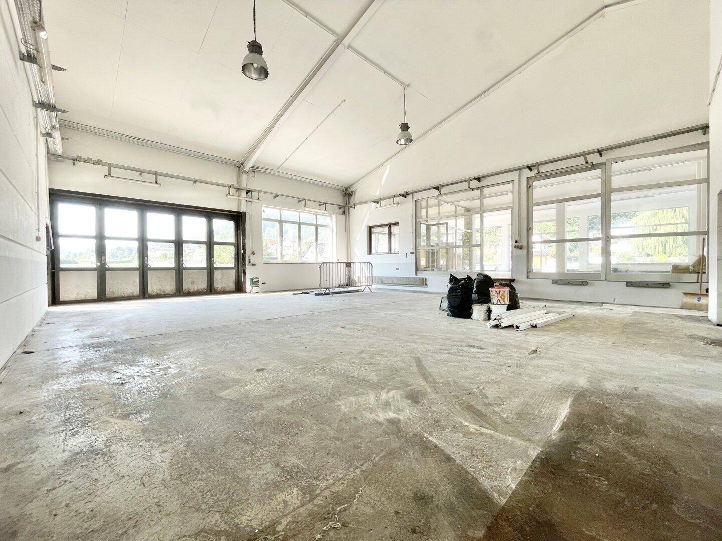 Weitläufige Industriehalle mit Betonboden, hohen Decken und großen Fenstern, bereit zur Neugestaltung.