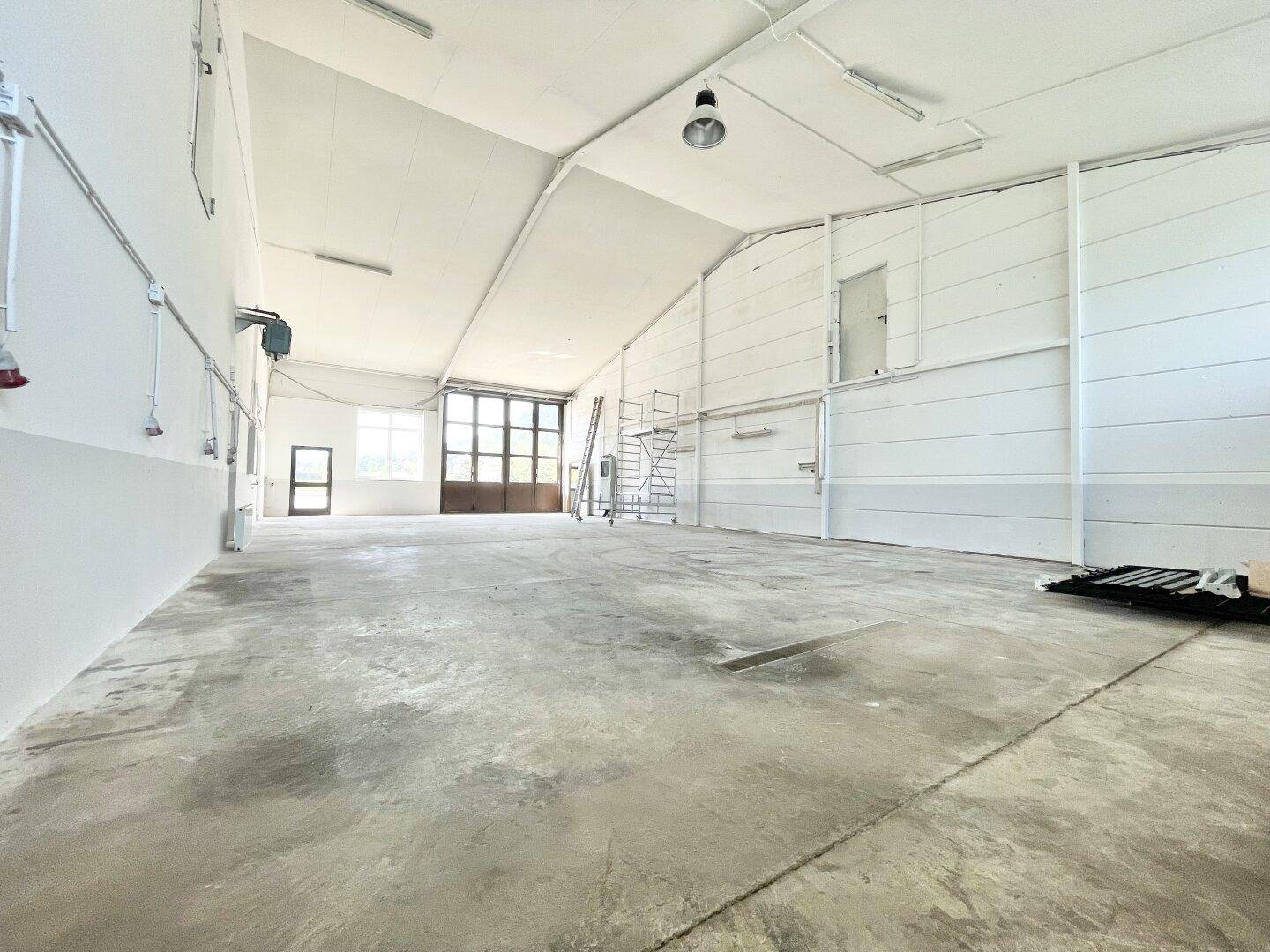 Geräumige, leere Lagerhalle mit hohen Decken, Betonboden und großem Rolltor am Ende.