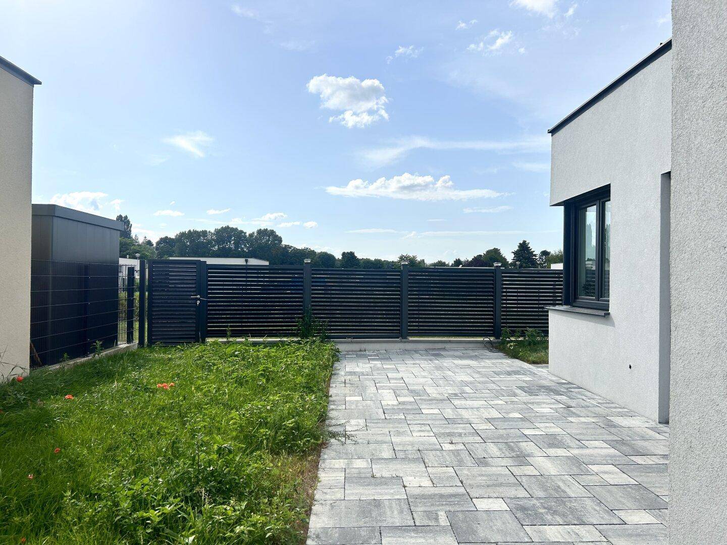 Gepflasterter Außenbereich mit Zaun und angrenzender Rasenfläche, ideal für Entspannung.