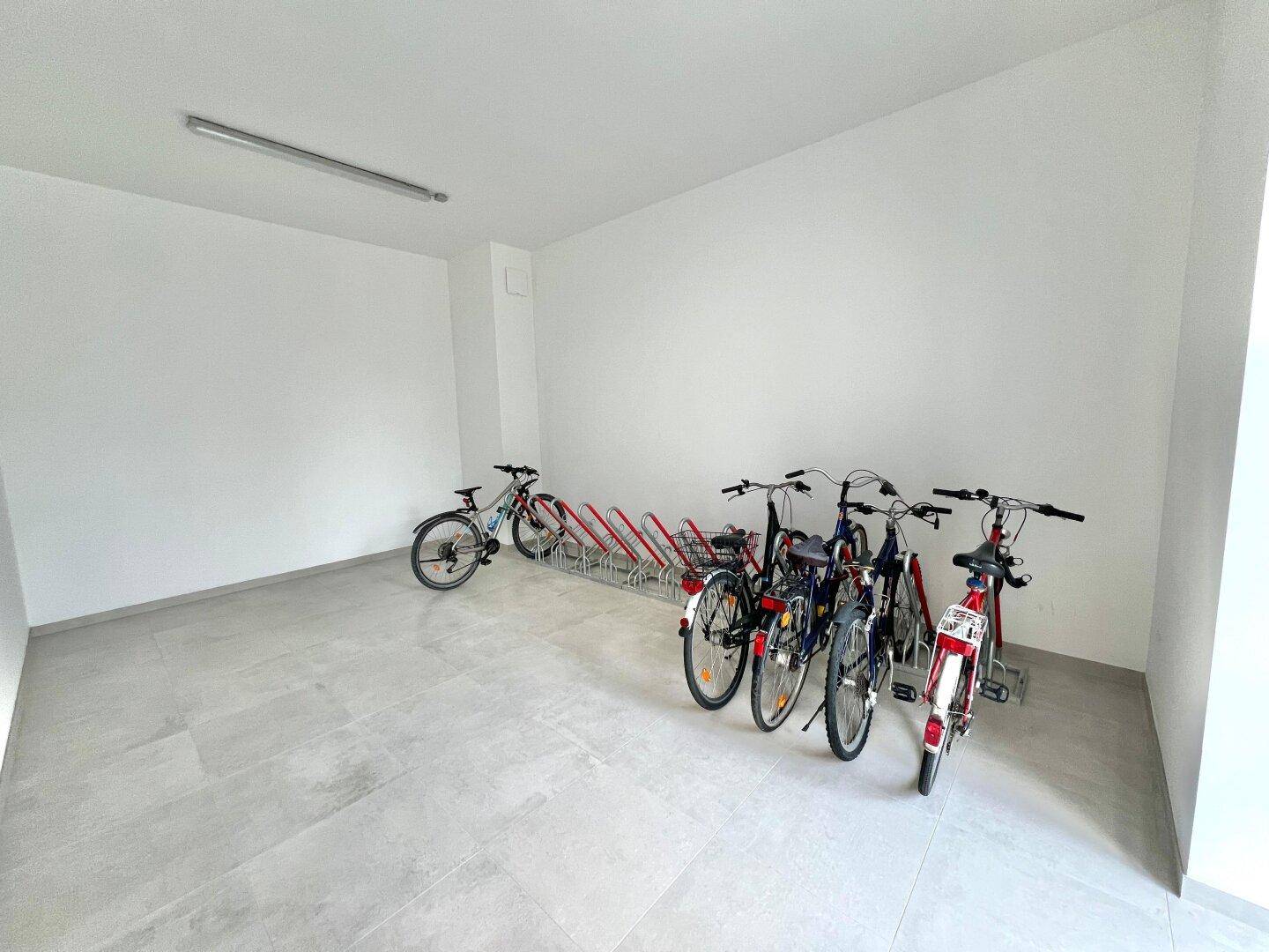 Geräumiger Fahrradabstellraum im Gebäude mit mehreren Fahrradständern und Fliesenboden.