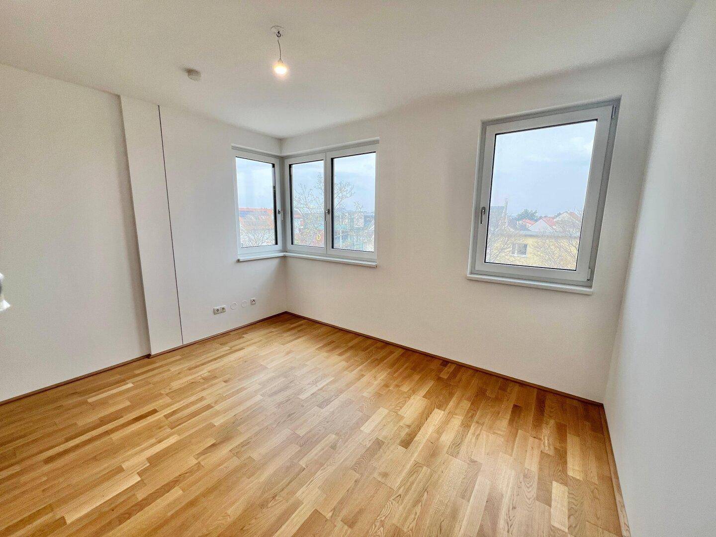Leeres Zimmer mit Holzboden und Fenstern über Eck, die eine weite Aussicht bieten.