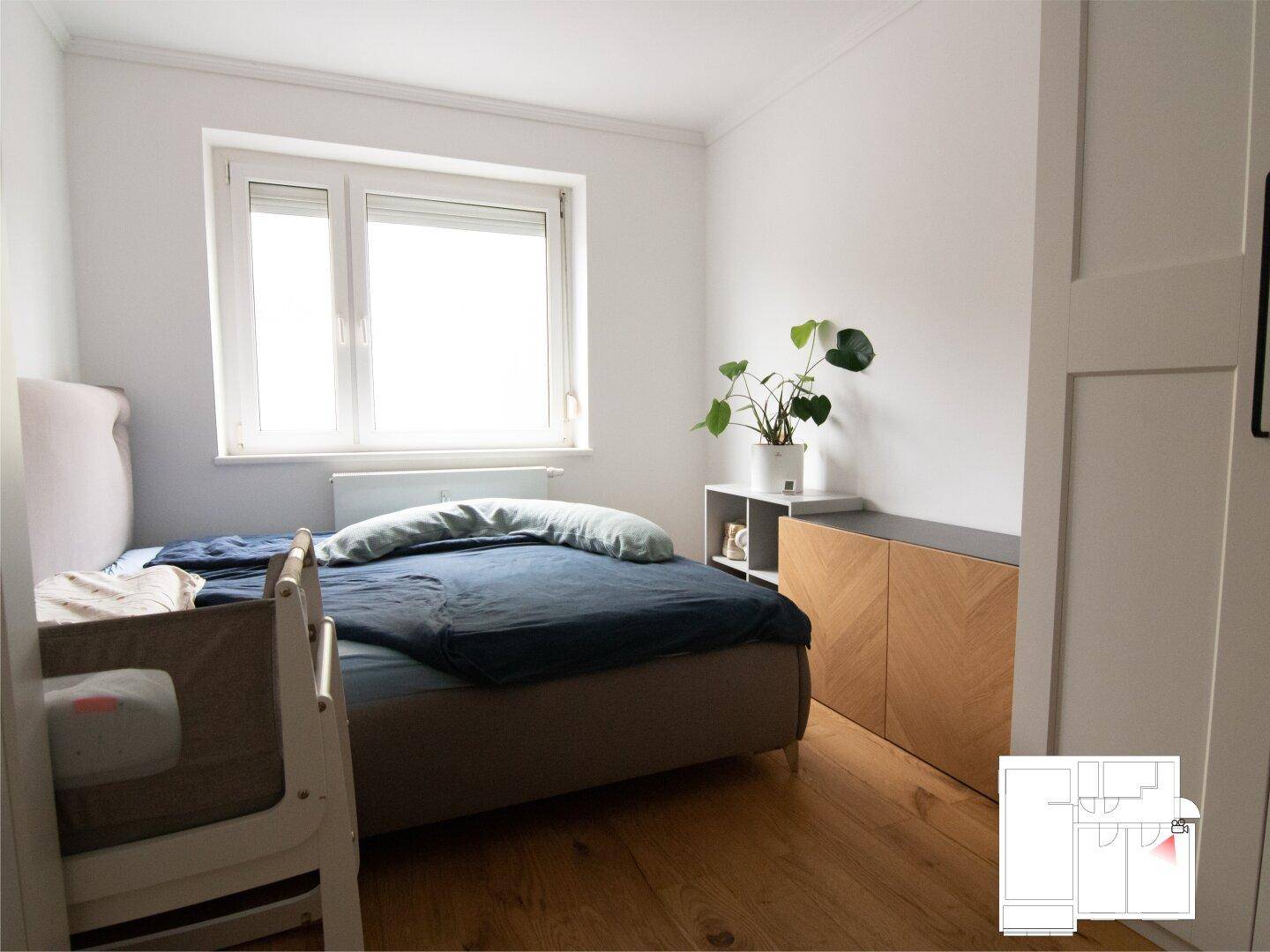 Gemütliches Schlafzimmer mit Doppelbett, Babybett und hellem Fenster.