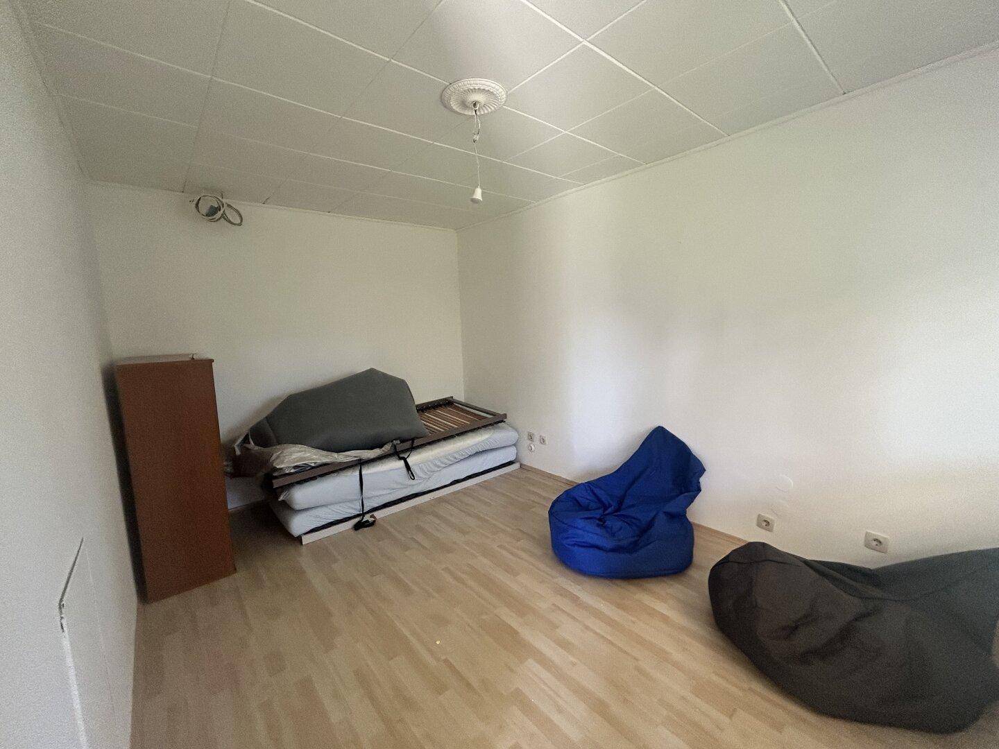 Einfaches Schlafzimmer mit Laminatboden und weißen Wänden, bereit zur individuellen Gestaltung.