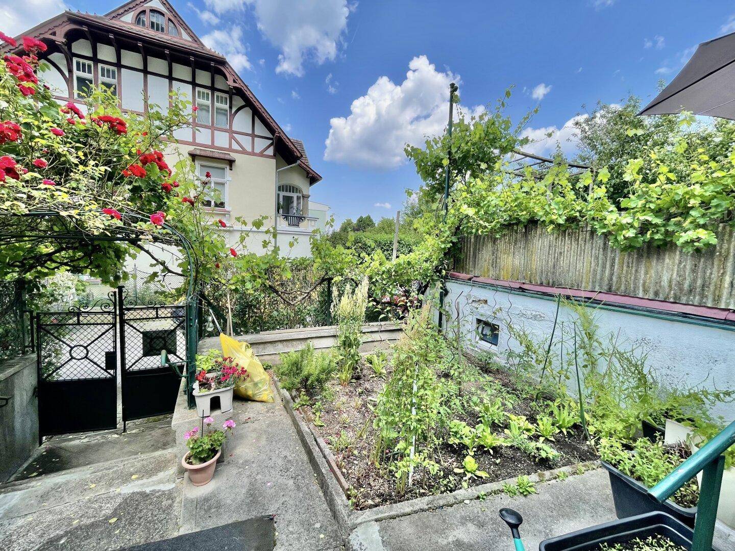 Kleiner Gartenbereich mit bepflanztem Beet und Blick auf die historische Fassade des Nachbarhauses.