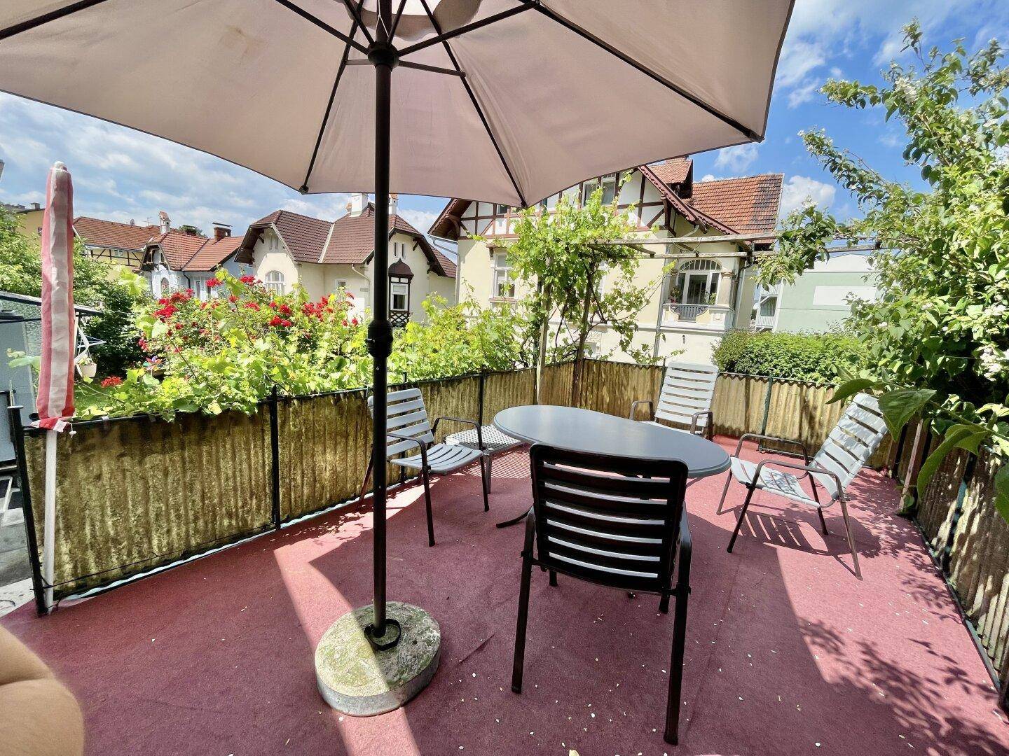 Gemütliche Terrasse mit Sonnenschirm und Gartenmöbeln, umgeben von Pflanzen und Blick auf die Nachbarschaft.