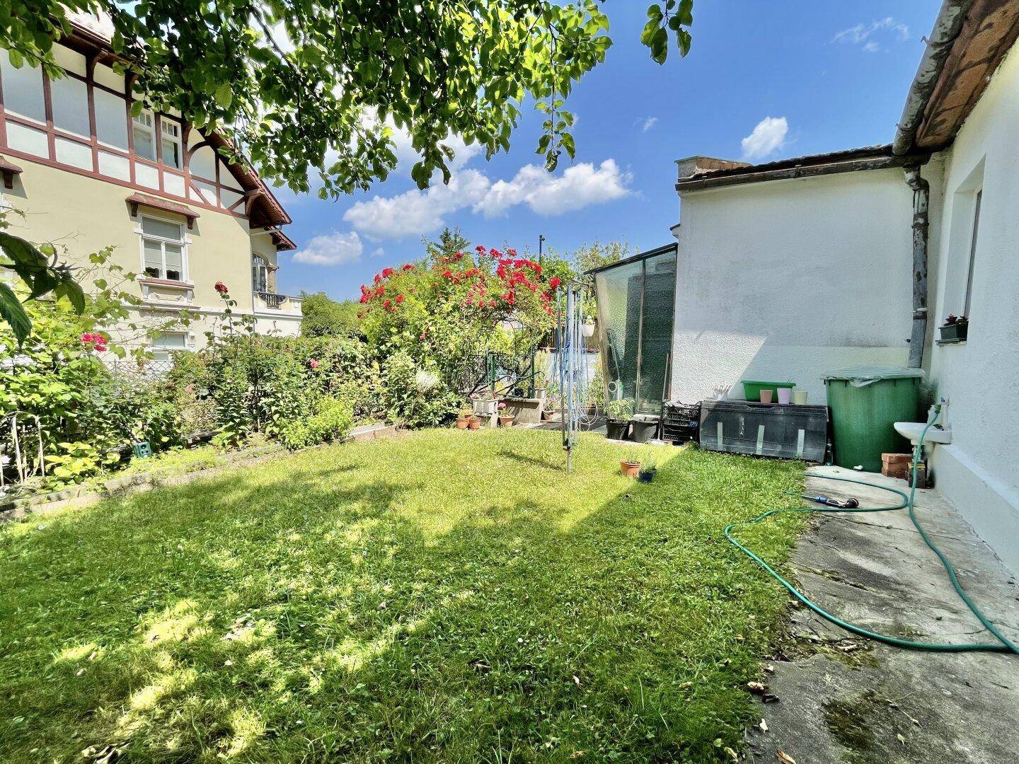 Gepflegter Rasenbereich im Garten neben dem Haus mit üppigem Grün und Bäumen im Hintergrund.