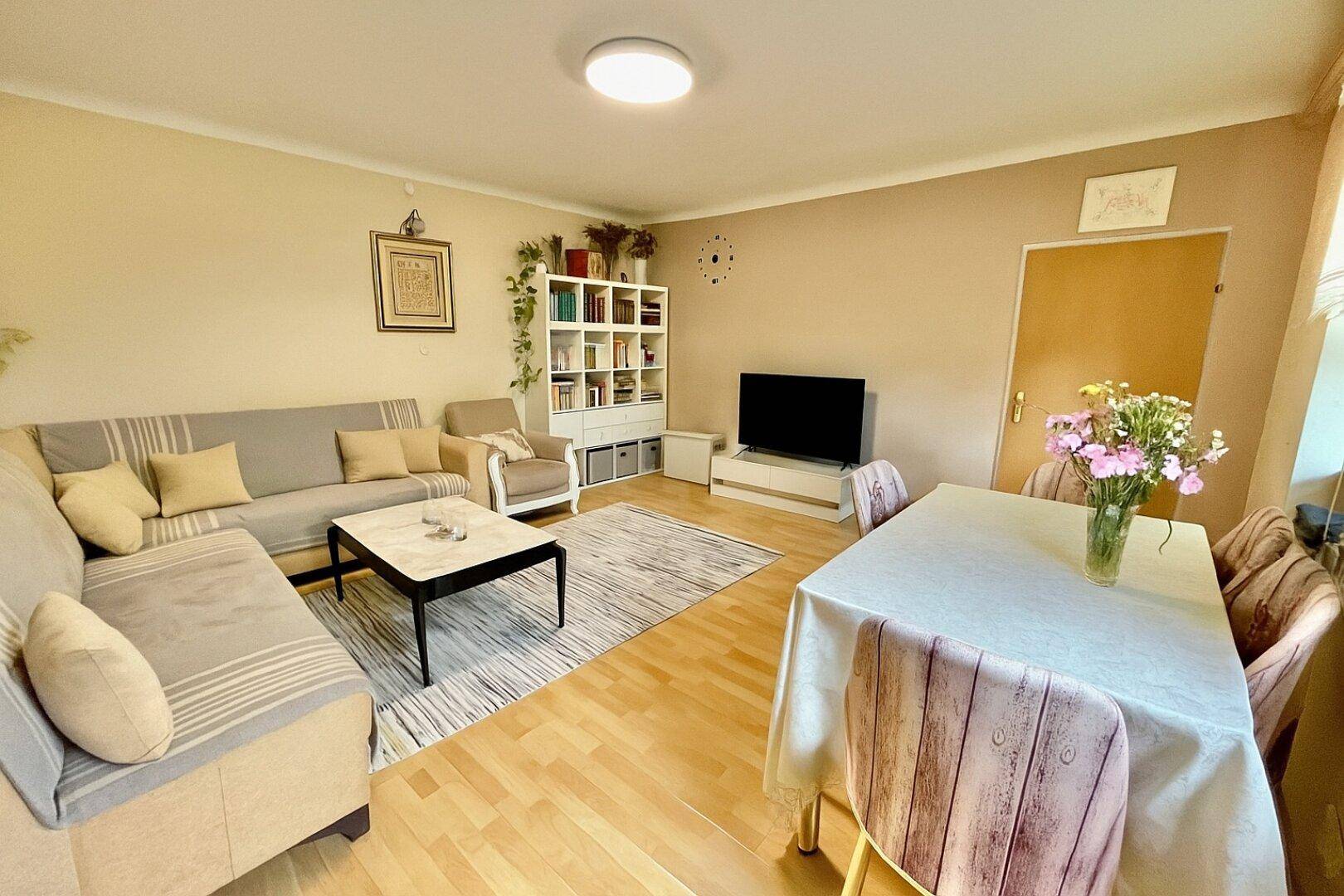 Kombinierter Wohn- und Essbereich mit Holzboden, Sofa und Esstisch in heller Farbgebung.