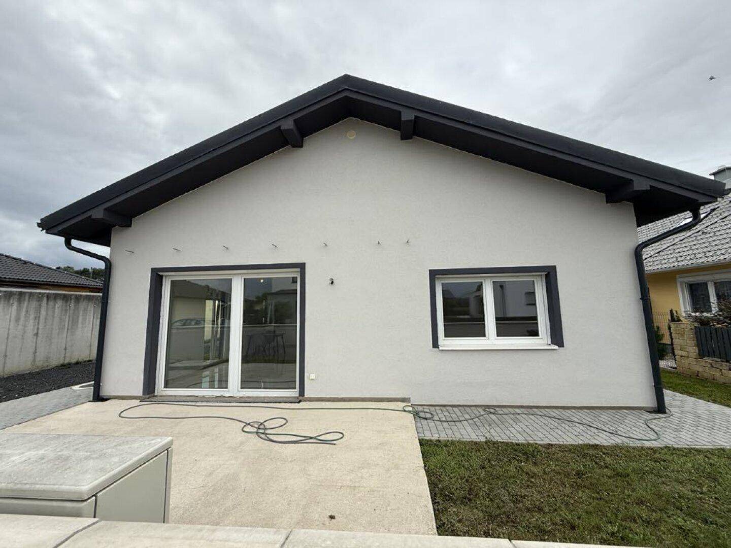 Außenansicht eines modernen Einfamilienhauses mit Terrasse und Gartenbereich unter bewölktem Himmel.