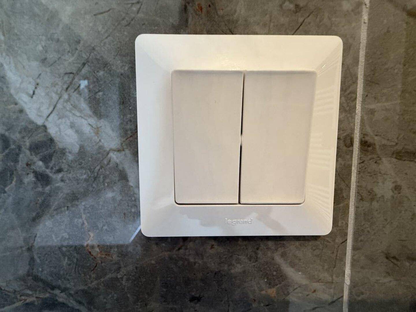 Detailaufnahme eines weißen Lichtschalters an einer dunkelgrauen Wand mit Marmoroptik.