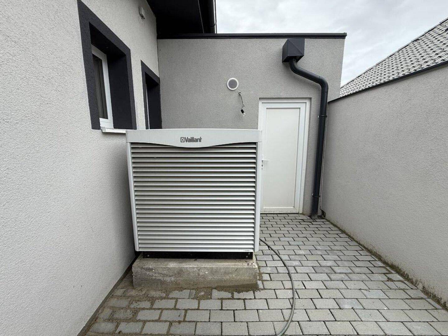 Außenansicht der Wärmepumpenanlage neben dem modernen Gebäude auf einem gepflasterten Bereich.