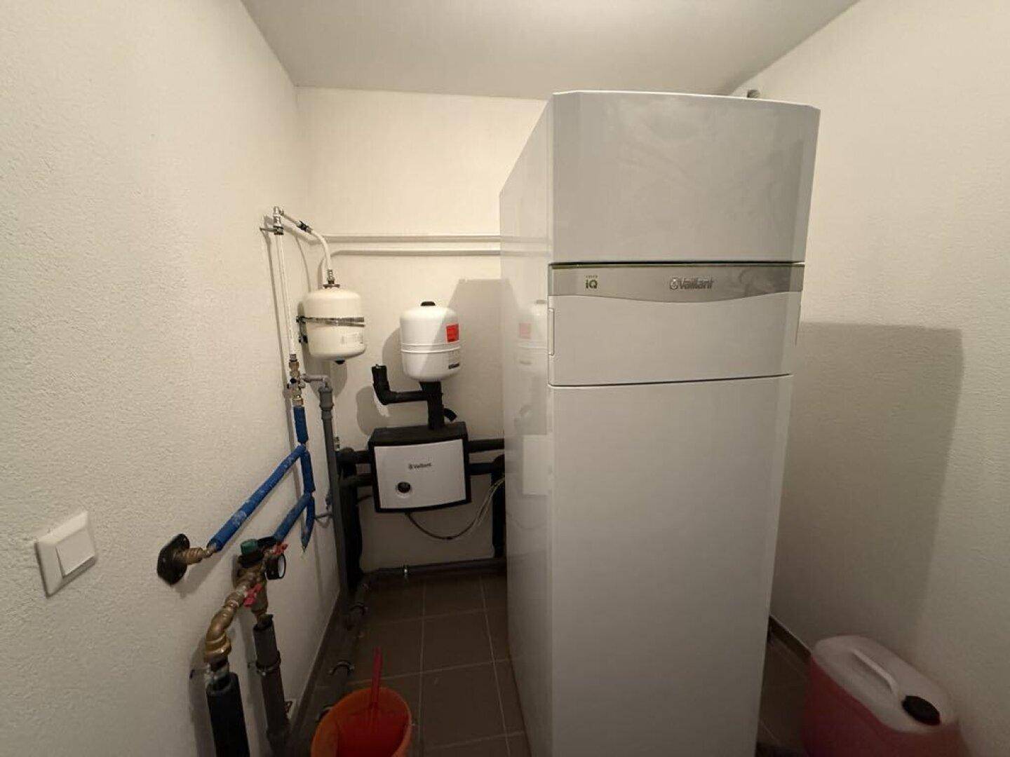 Innenansicht eines Hauswirtschaftsraums mit moderner Wärmepumpenanlage und sichtbaren Rohrleitungen.