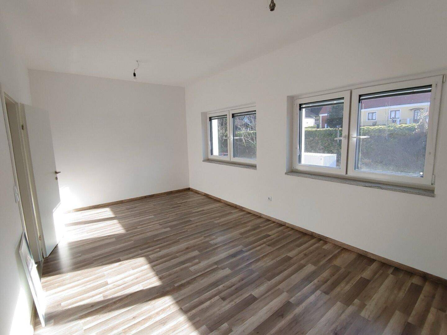 Helles, unmöbliertes Schlafzimmer mit Laminatboden, weißen Wänden und zwei Fenstern.
