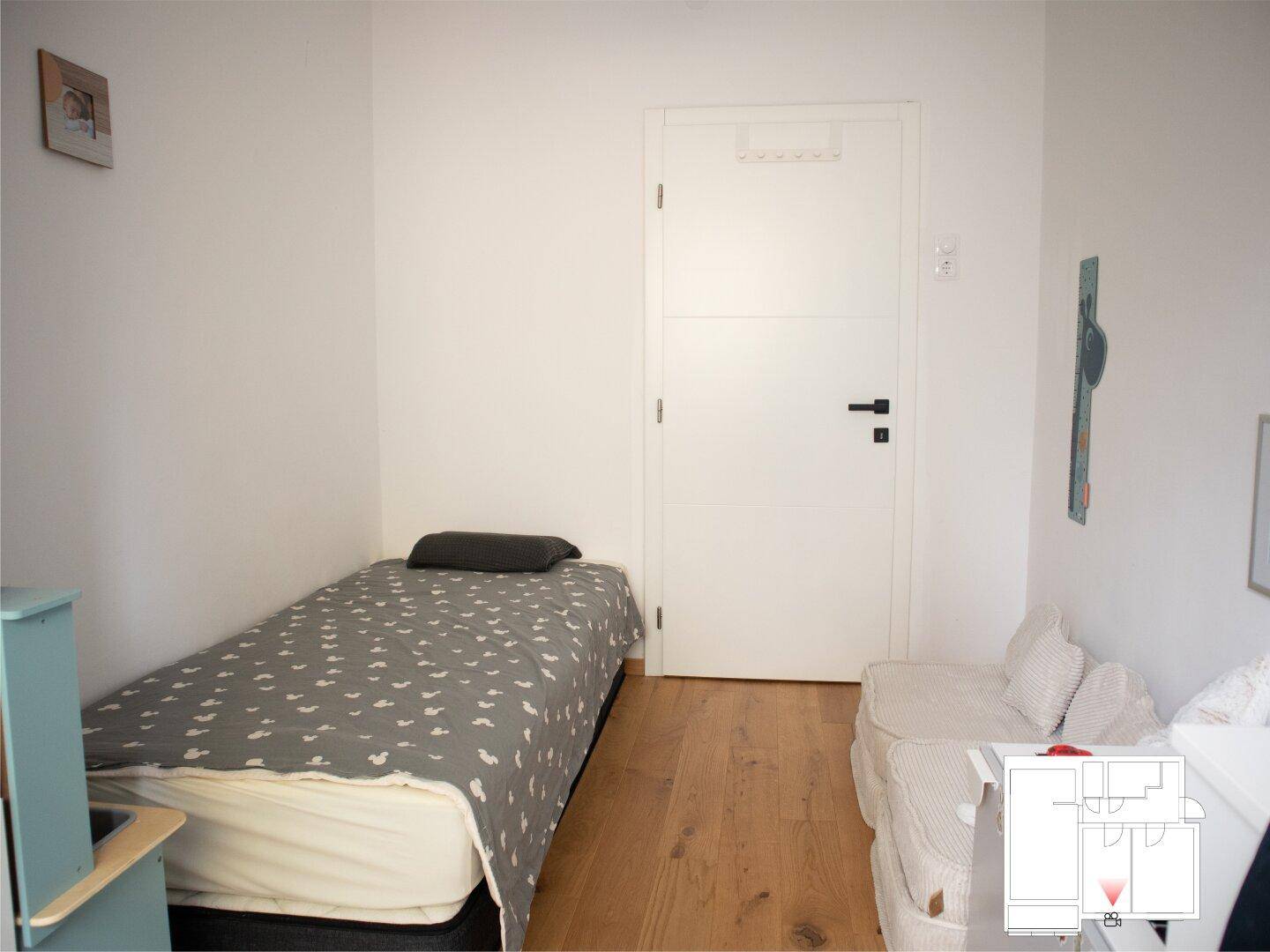 Kinderzimmer mit Einzelbett, Holzboden und weißer Tür.