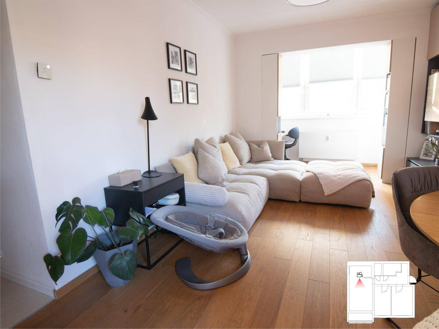 Helles Wohnzimmer mit beigem Ecksofa, Holzboden und Blick auf den Balkon.