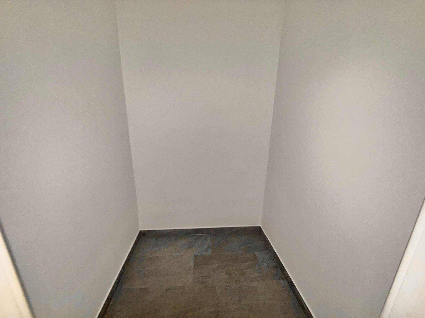 Leerer Abstellraum mit grauen Fliesen und weißen Wänden.