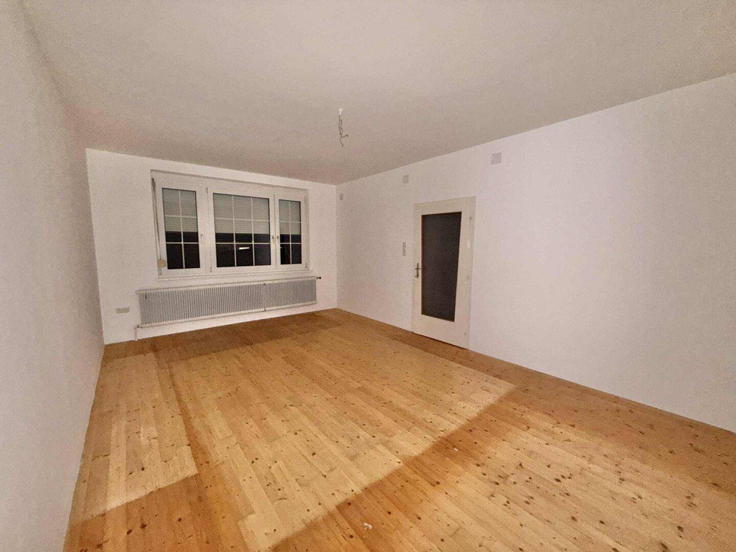 Geräumiger, heller Raum mit Holzfußboden und großem Fenster mit Heizkörper darunter.