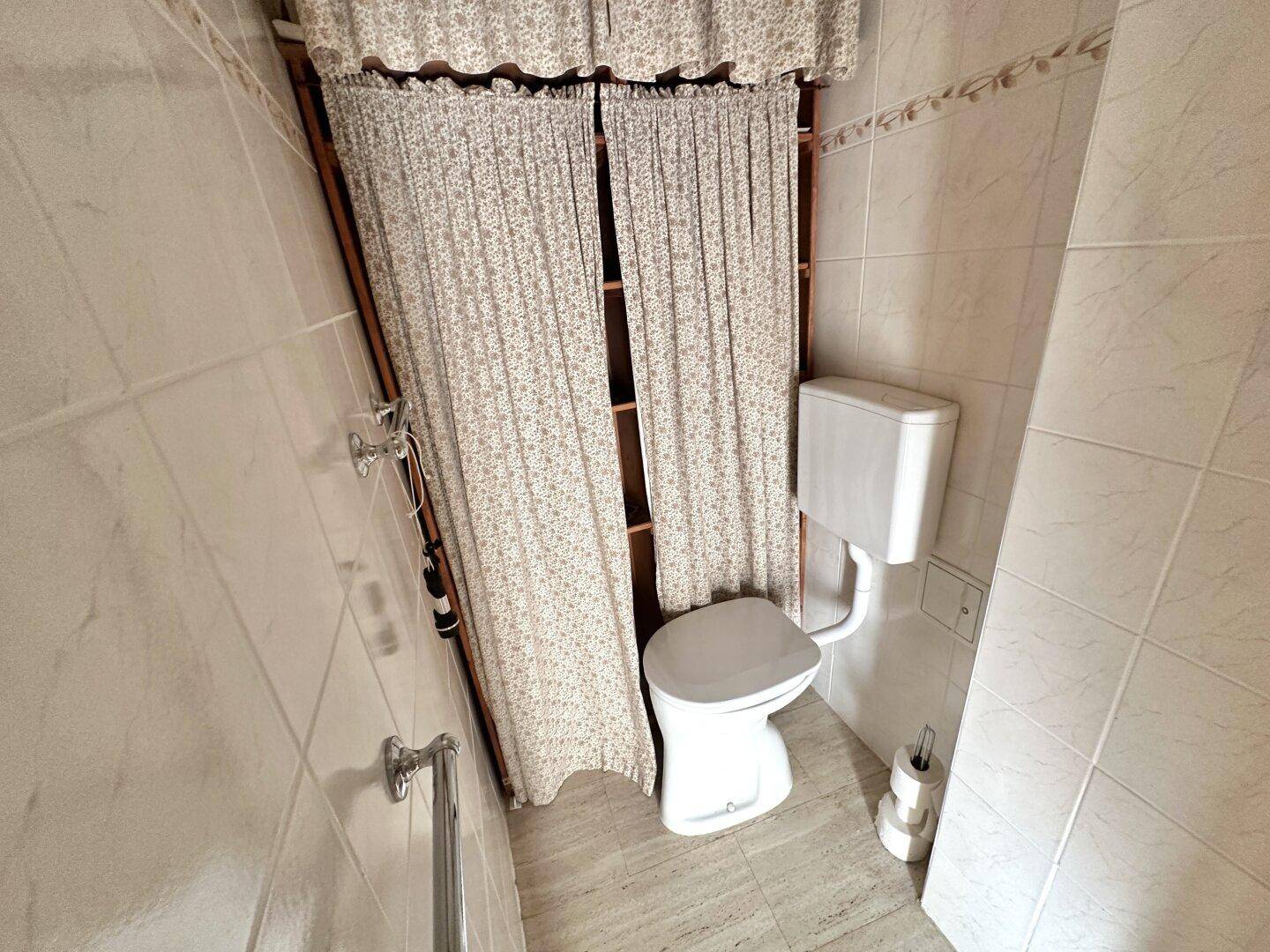 Separates WC mit Wandtoilette und Vorhängen, in einem einfachen, funktionalen Design.