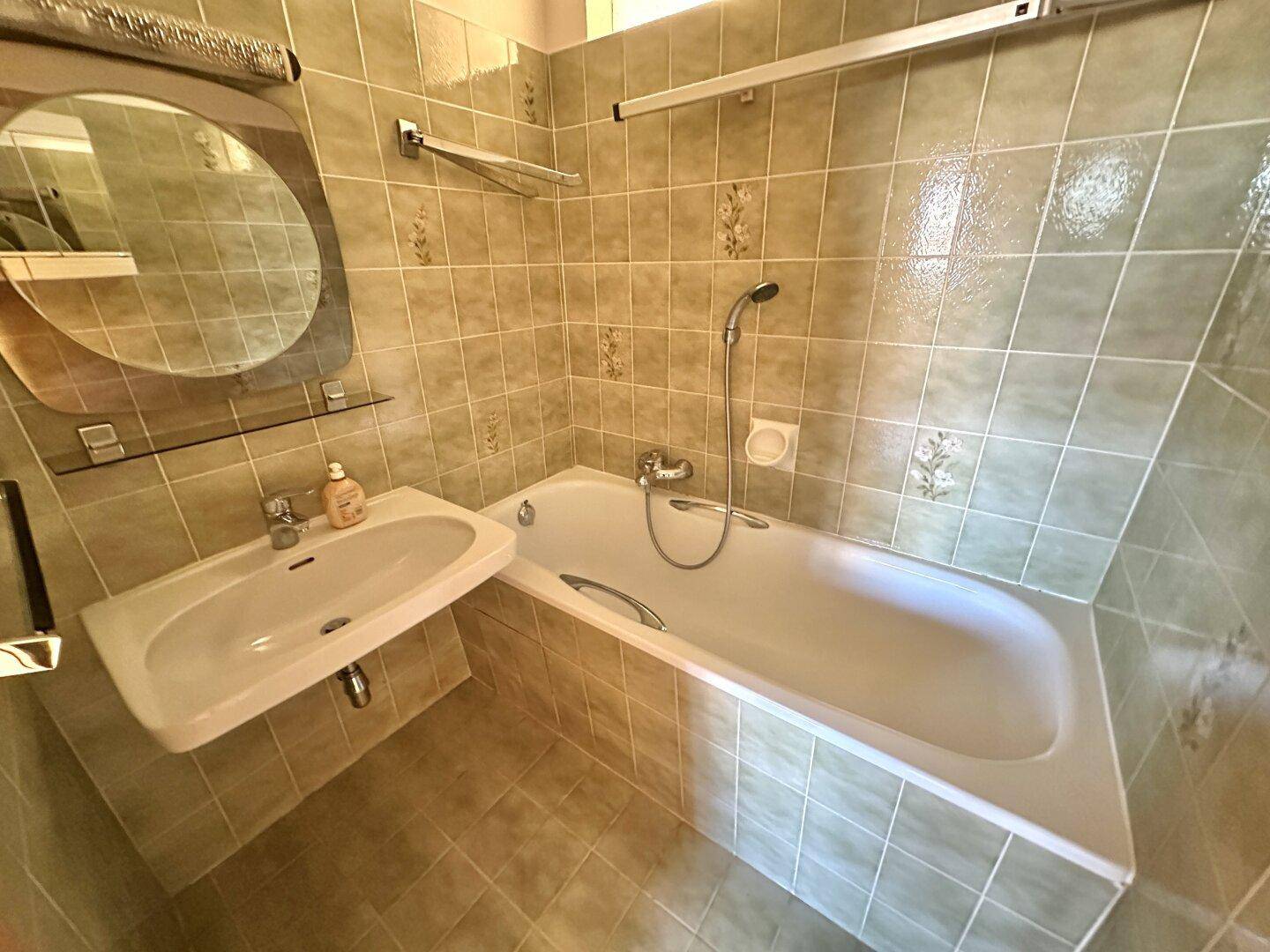 Badezimmer mit Badewanne, Waschbecken und hellgrünen Fliesen, in gutem Zustand.