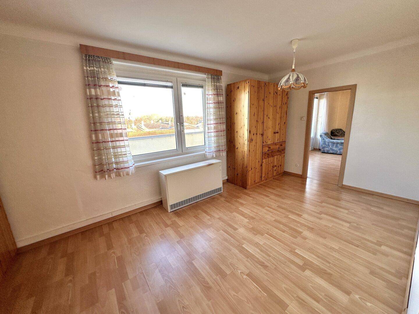 Helles Schlafzimmer mit Laminatboden, großem Fenster und einem traditionellen Holzschrank.
