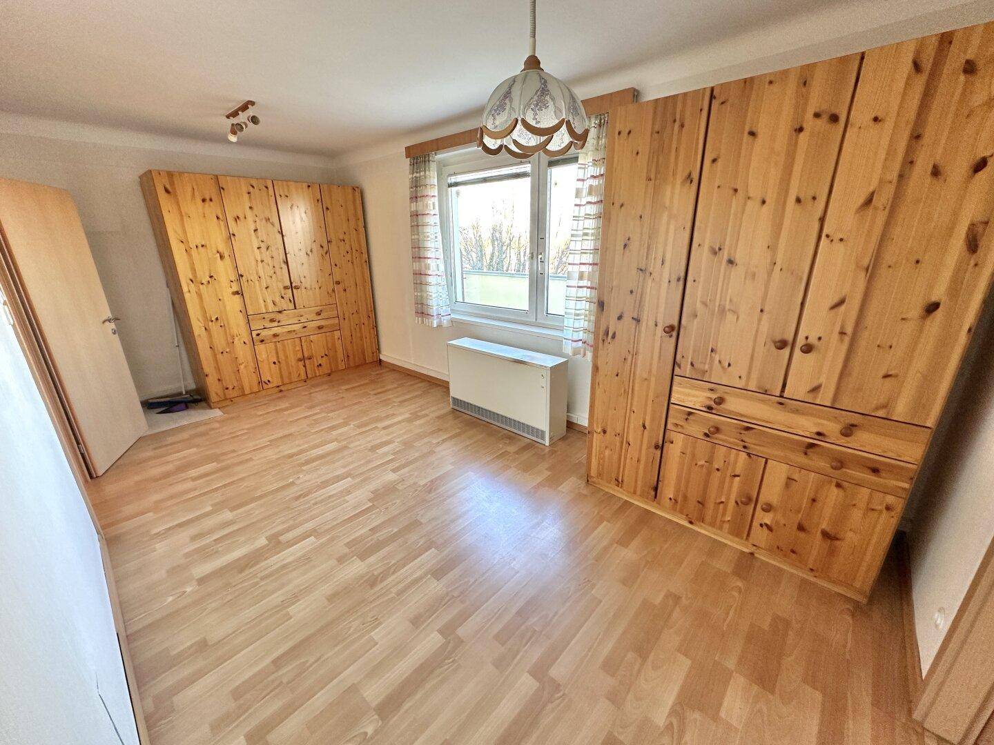 Geräumiges Schlafzimmer mit zwei großen Holzschränken, Laminatboden und viel Tageslicht.