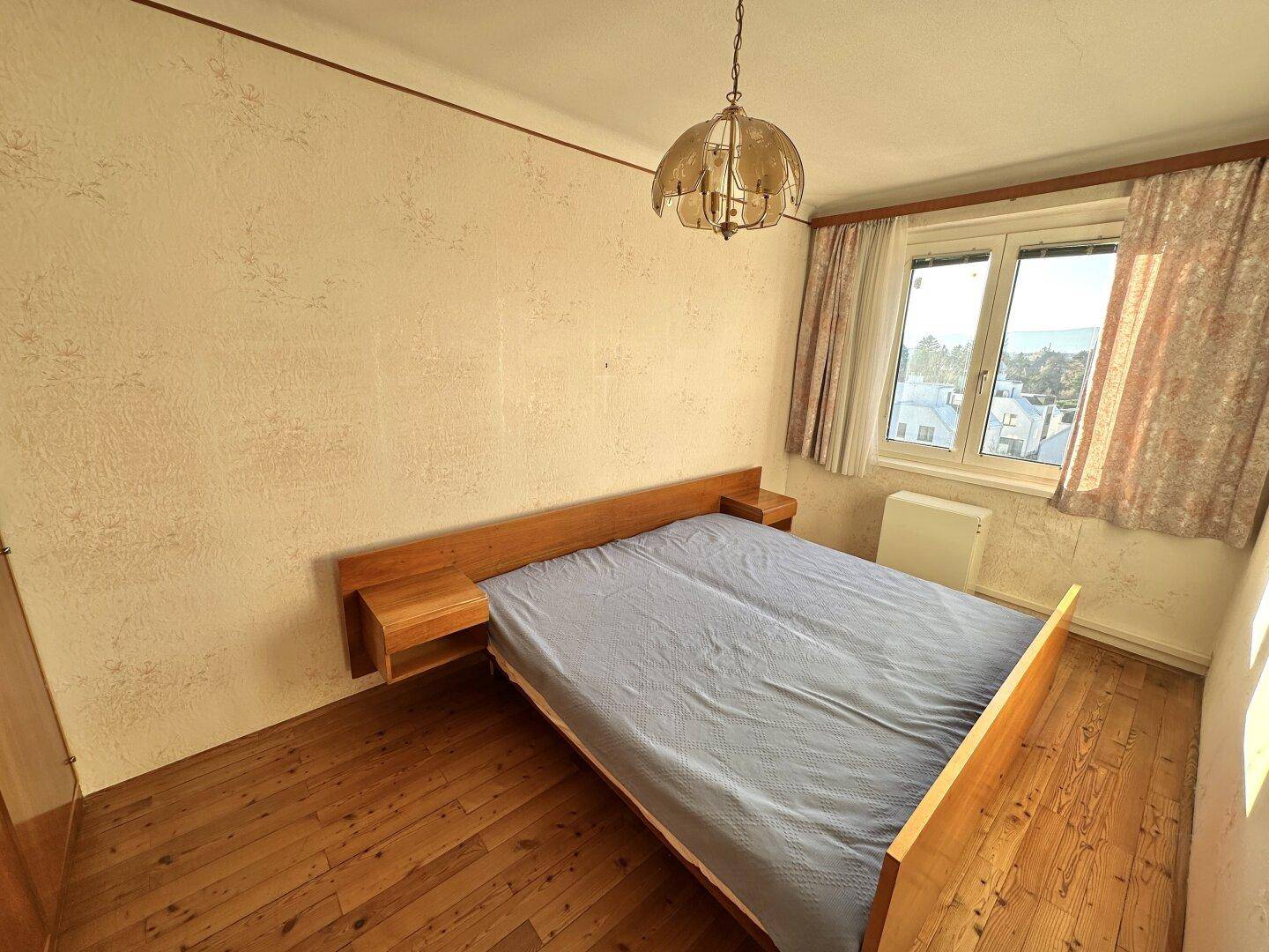 Gemütliches Schlafzimmer mit Holzbett, Laminatboden und einem Fenster für natürliche Belichtung.