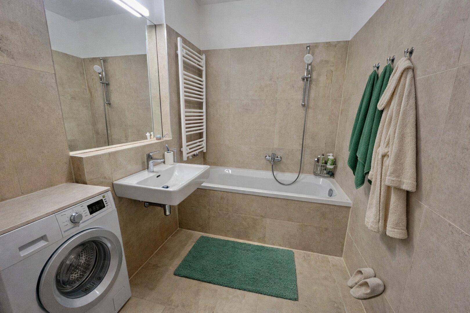 Modernes Badezimmer mit Badewanne, Waschbecken, beheiztem Handtuchhalter und Waschmaschine.
