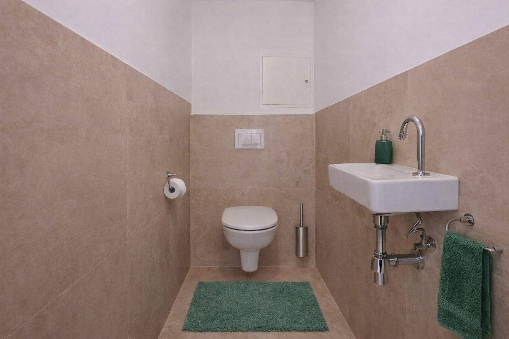 Kleines Gäste-WC mit Wand-WC und modernem Waschbecken in beigefarbenen Fliesen.