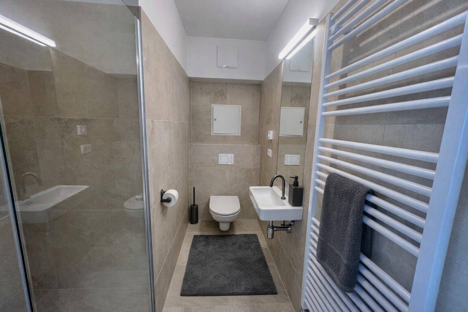 Modernes Badezimmer mit ebenerdiger Dusche, Wand-WC und beheiztem Handtuchhalter.
