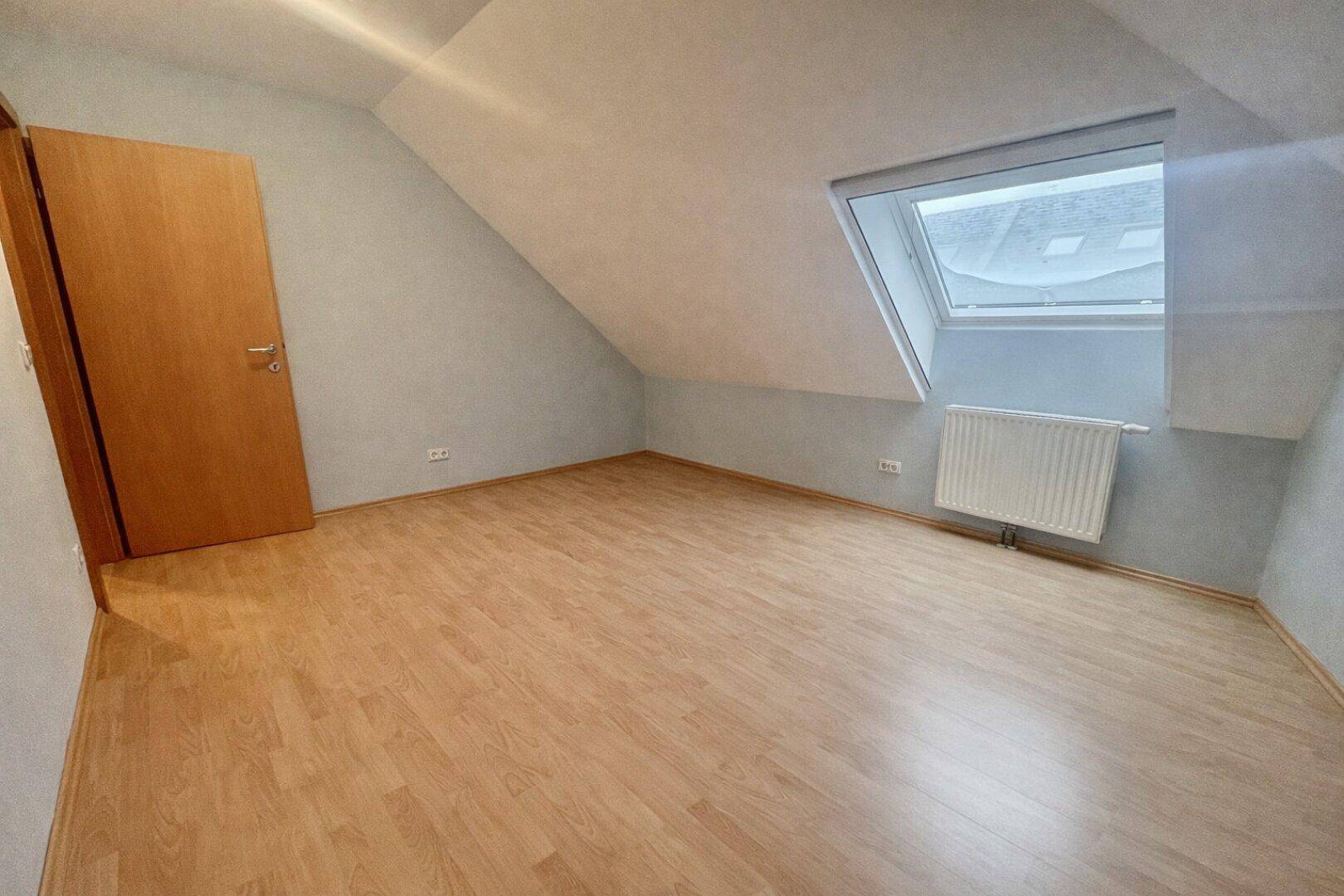 Helles Dachzimmer mit Laminatboden, Dachfenster und schrägen Wänden, unmöbliert und geräumig.