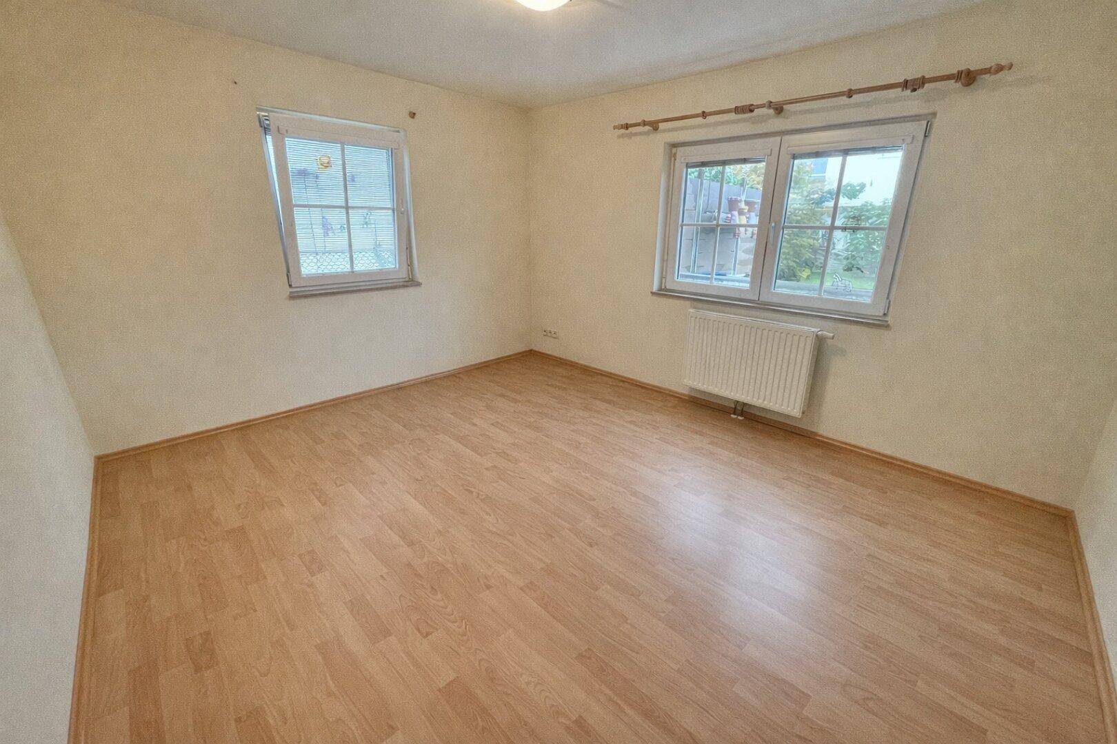 Geräumiges Schlafzimmer mit Laminatboden und zwei Fenstern, die viel Tageslicht hereinlassen.