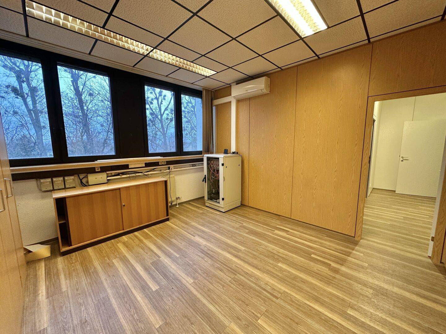Büro mit Holzvertäfelung, Laminatboden und einem Serverschrank neben dem Fenster.