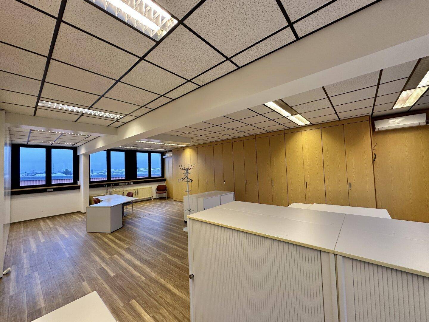 Weitläufiges Büro mit vielen Fenstern, integrierten Schränken und flexiblen Arbeitsbereichen.
