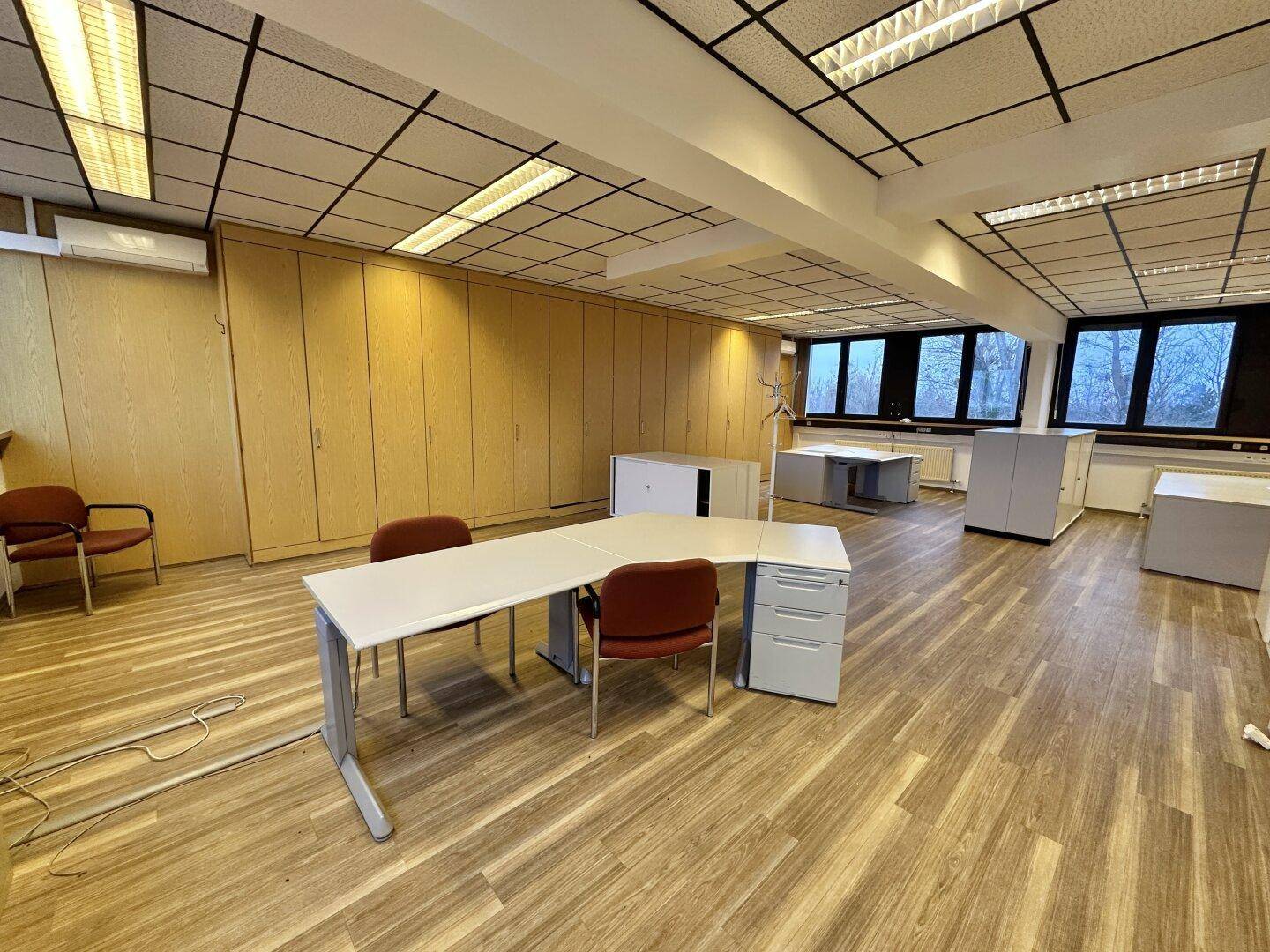 Großes Großraumbüro mit mehreren Arbeitsplätzen, Holzvertäfelung und Laminatboden.