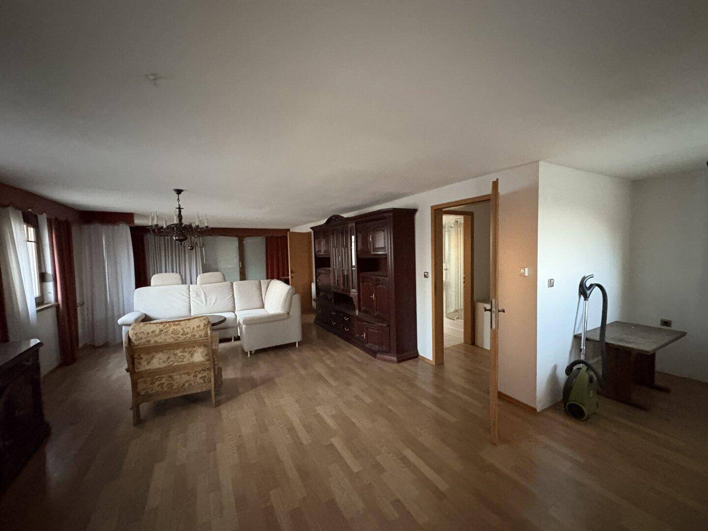 Geräumiges Wohnzimmer mit Parkettboden, traditionellen Holzmöbeln und heller Couch.