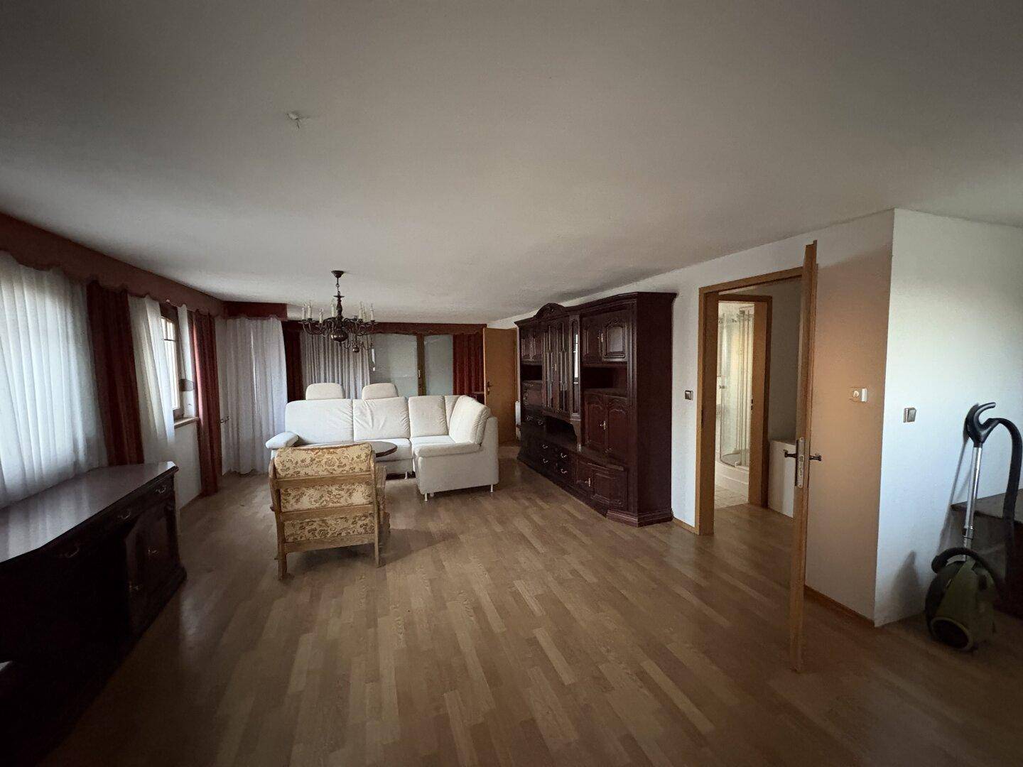 Helles Wohnzimmer mit Parkettboden, klassischem Mobiliar und Zugang zu weiteren Räumen.