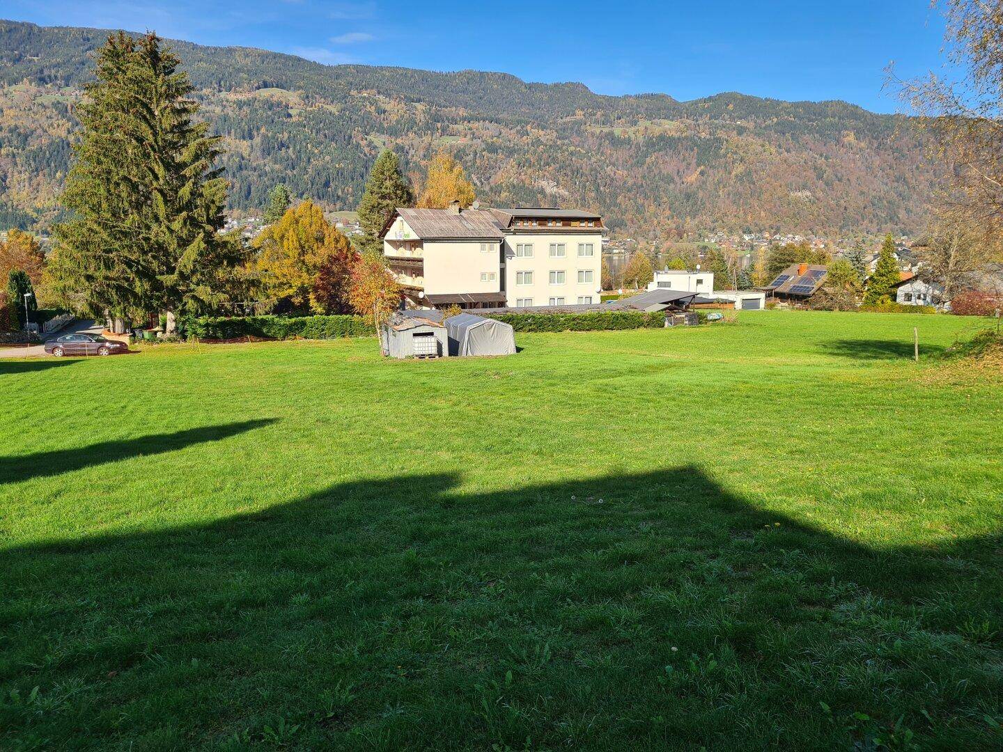 Mehrstöckiges Gebäude umgeben von einer weiten grünen Wiese mit Bergen im Hintergrund an einem sonnigen Tag.