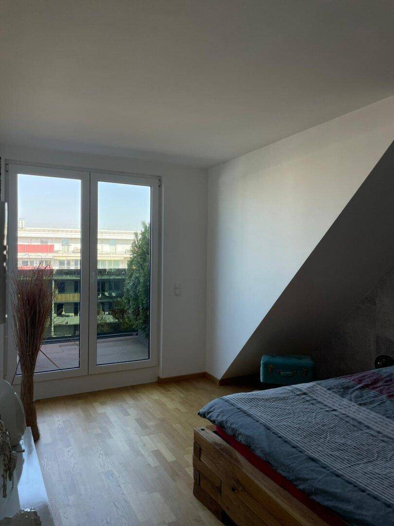 Helles Schlafzimmer mit Holzboden und direktem Zugang zur Terrasse, unter einer Dachschräge.