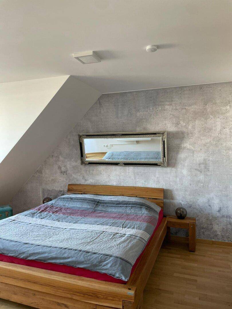 Schlafzimmer mit Holzbett, gemusterter Tapete und Dachschräge, gemütlich und modern eingerichtet.