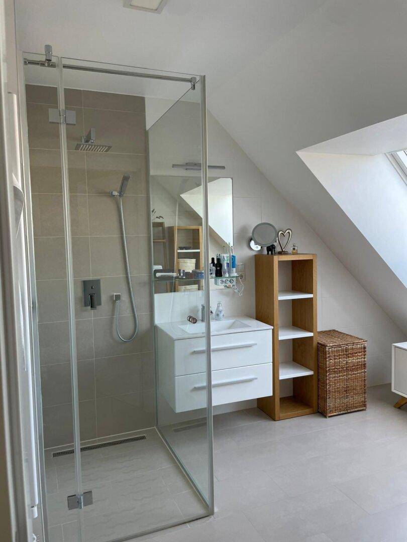 Modernes Badezimmer mit begehbarer Dusche, Waschtisch und Dachfenster für natürliches Licht.