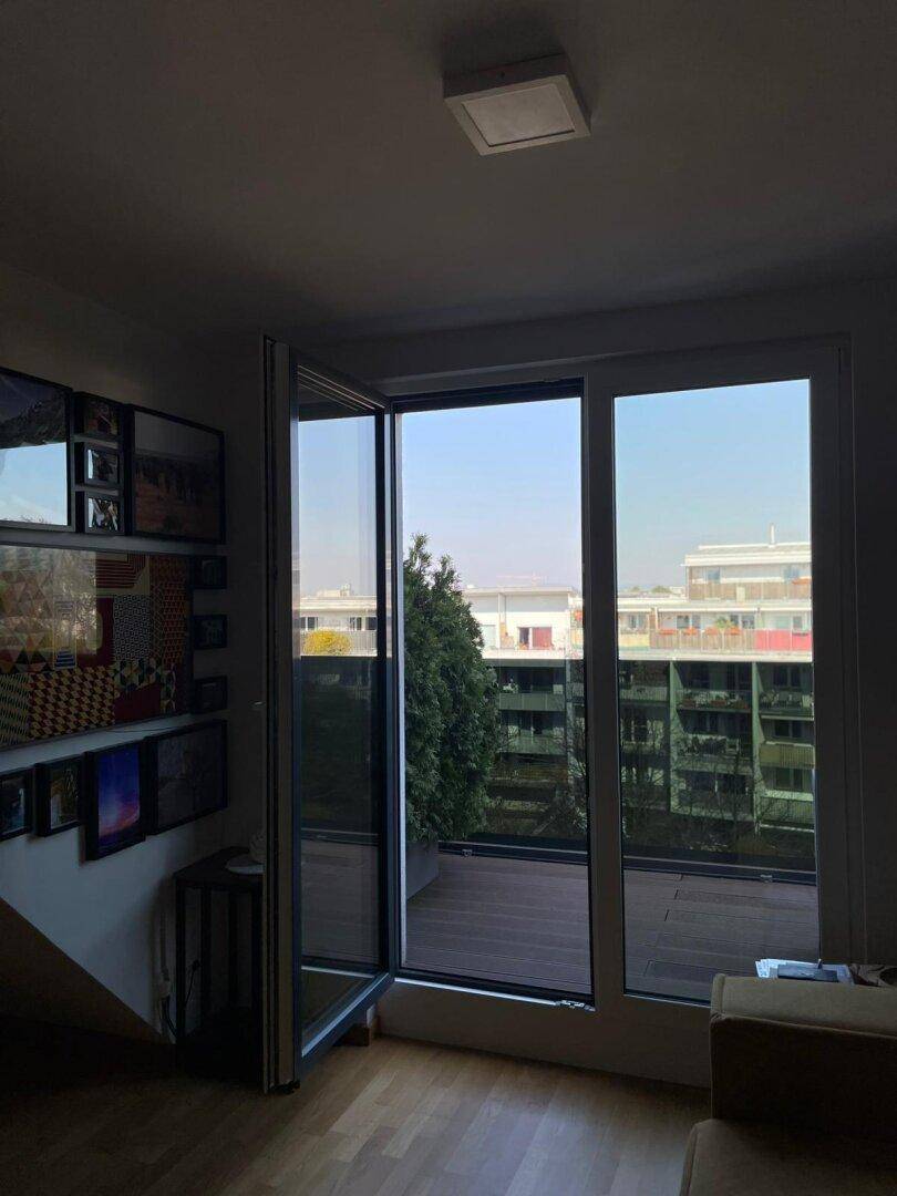 Wohnbereich mit Zugang zur Terrasse und Blick auf die umliegenden Gebäude, hell und geräumig.