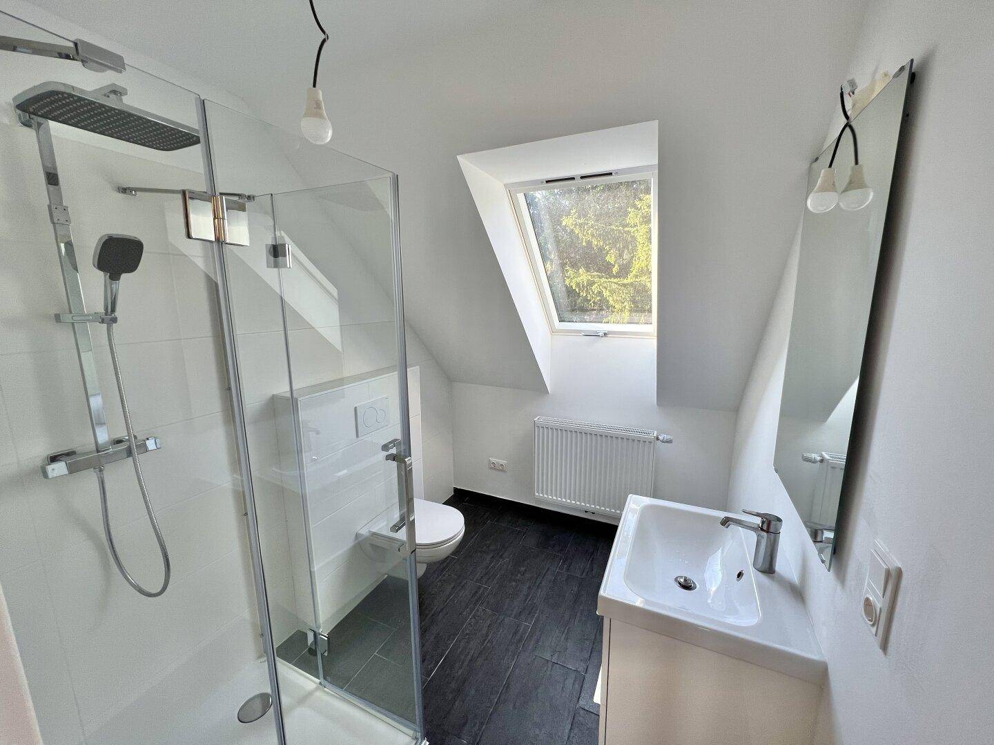 Modernes Badezimmer im Dachgeschoss mit begehbarer Dusche, WC und Dachfenster.