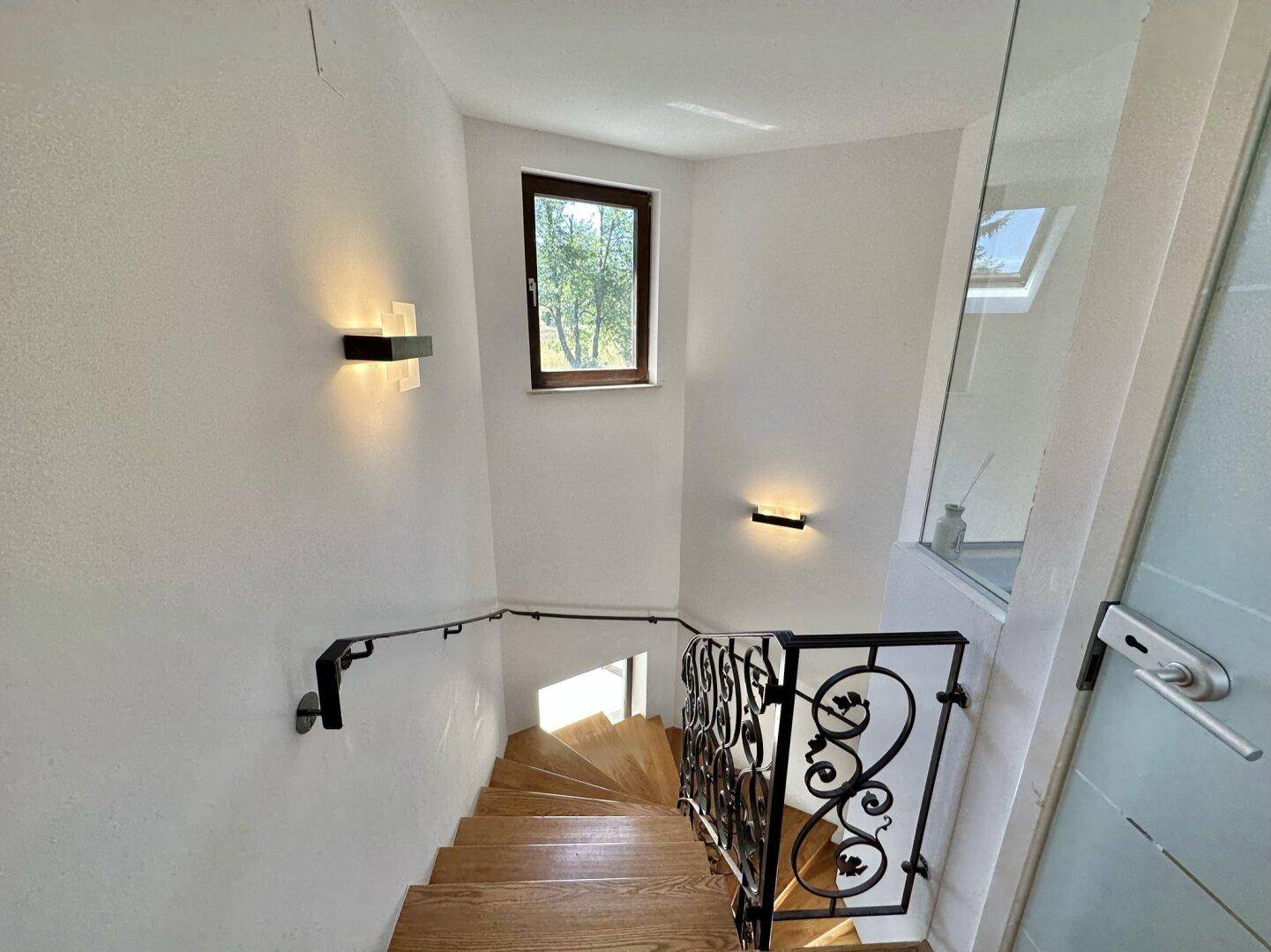 Elegantes Treppenhaus mit Holzstufen und schmiedeeisernem Geländer, gut beleuchtet.