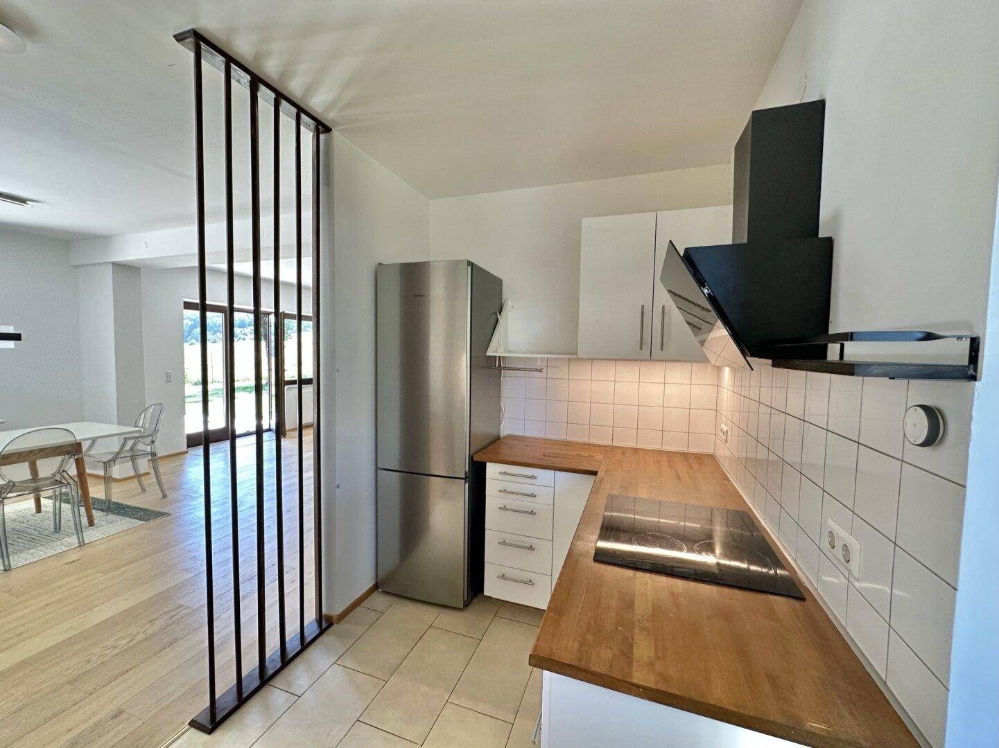 Funktionale Küche mit weißen Schränken, Kühlschrank und Kochfeld, offen zum Essbereich.