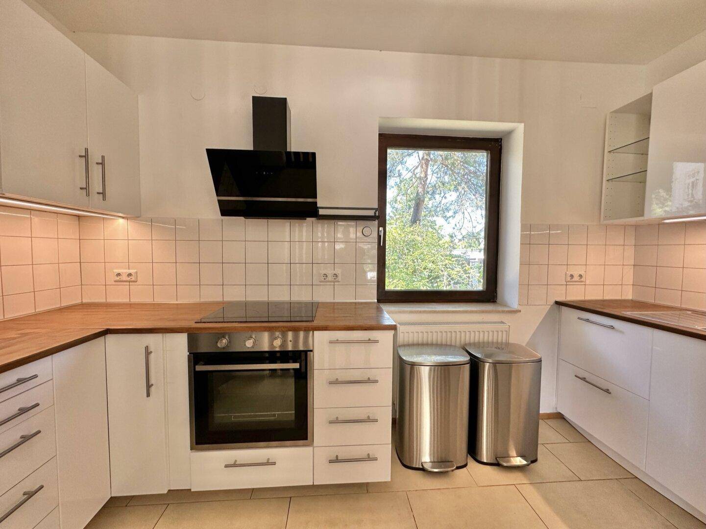 Moderne Einbauküche mit weißen Schränken, Holz-Arbeitsplatte und Induktionskochfeld.