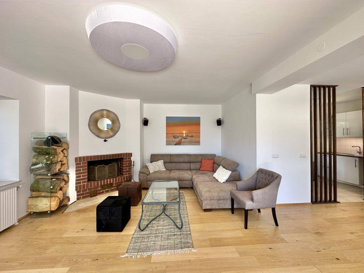 Gemütliches Wohnzimmer mit Kamin, Ecksofa und Holzboden, offen zur Küche.